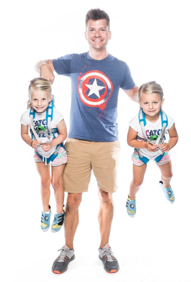 A man gripping two happy toddler climbers by their safety harnesses