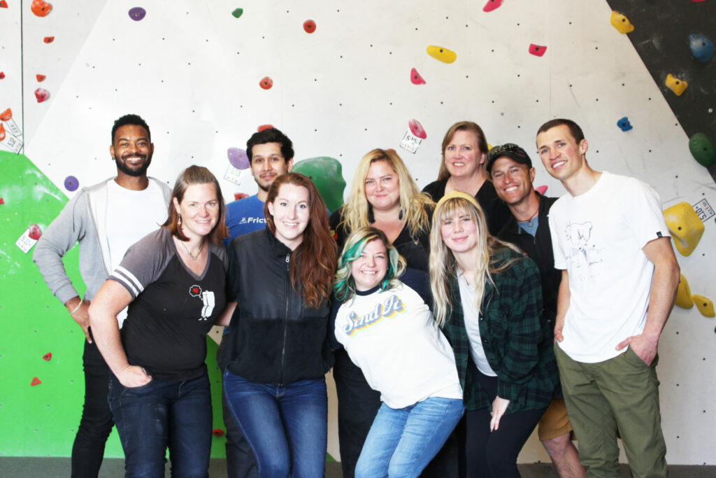 A group of diverse and happy people standing in front of a bouldering wall