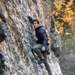 Man in black hoodie climbing a mountain with the aid of a rope