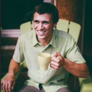 Man sitting on a chair while holding a cup of coffee and smiling brightly