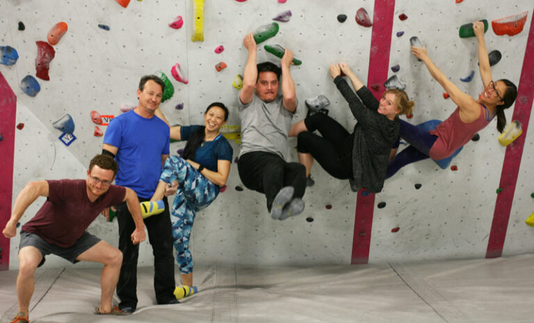 A group of happy and diverse people in front of a climbing wall.