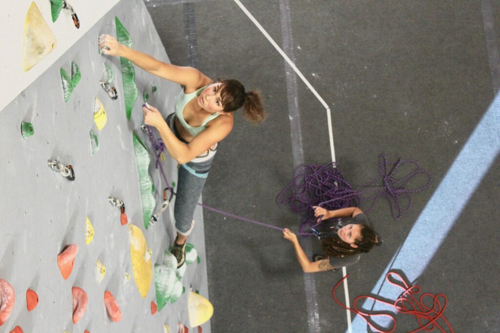 Lady climbing a bouldering wall in the company of a belayer