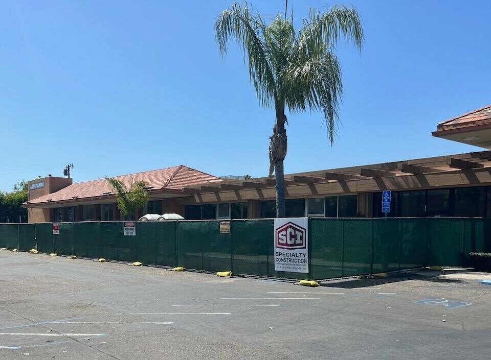 External image of the construction fence surrounding the building at the site of The Pad Santa Barbara. A palm tree stretches out into the blue Central Coast sunny sky.